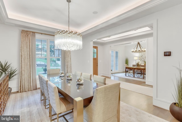 dining area featuring a chandelier, a raised ceiling, wood finished floors, and ornamental molding