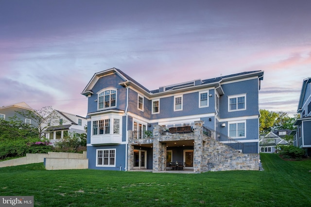 back of property at dusk with a patio area, stairs, stone siding, and a lawn