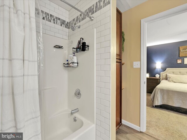 ensuite bathroom with baseboards, wood finished floors, ensuite bath, and shower / bathtub combination with curtain