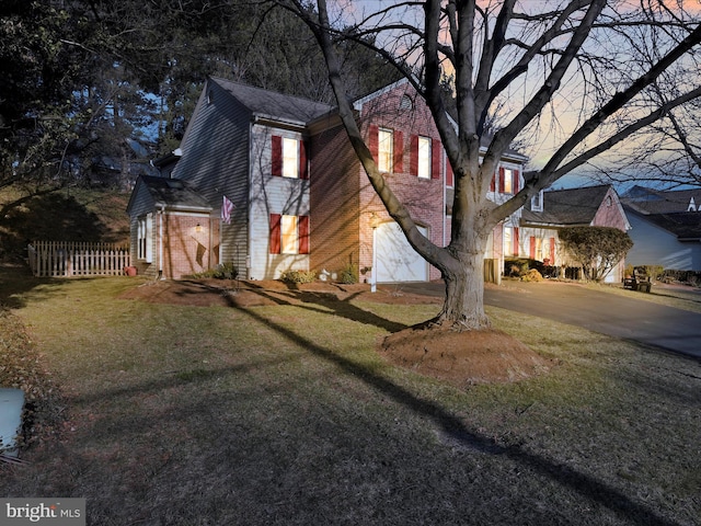 property exterior at dusk with a yard, driveway, brick siding, and fence