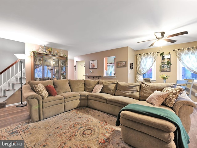 living room featuring ceiling fan, stairs, baseboards, and wood finished floors