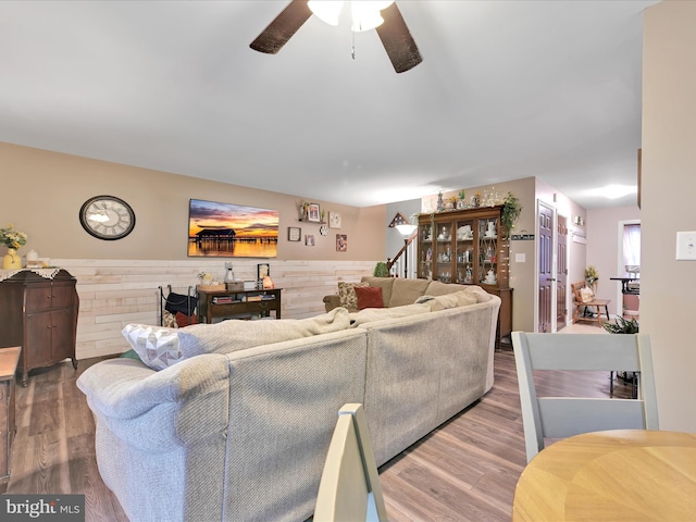 living room with ceiling fan, wooden walls, a wainscoted wall, wood finished floors, and stairs