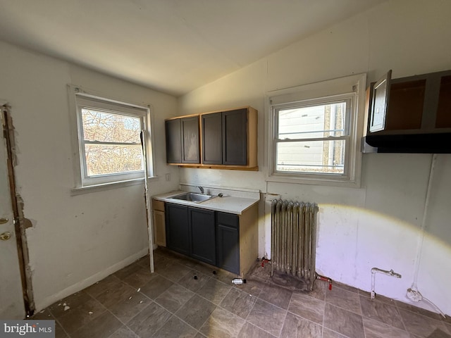 kitchen featuring radiator, baseboards, light countertops, vaulted ceiling, and a sink