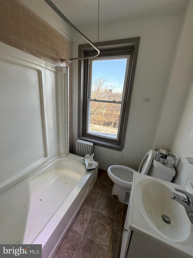 bathroom featuring toilet, stone tile floors, radiator heating unit, and vanity