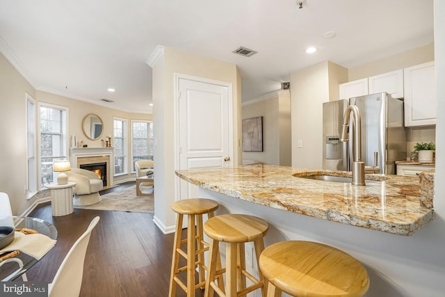 kitchen with visible vents, ornamental molding, light stone counters, dark wood-style floors, and white cabinets