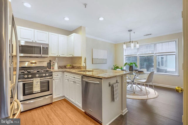 kitchen with a sink, light wood-style floors, a peninsula, appliances with stainless steel finishes, and white cabinets