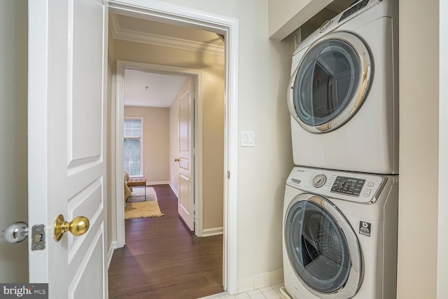 laundry room featuring wood finished floors, baseboards, stacked washing maching and dryer, laundry area, and crown molding