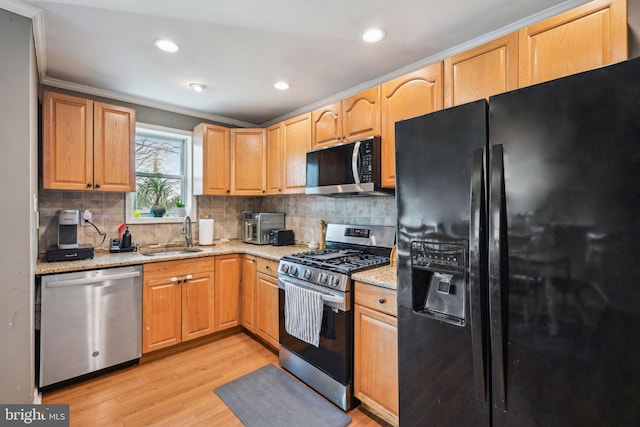 kitchen with light wood finished floors, stainless steel appliances, backsplash, a sink, and light stone countertops