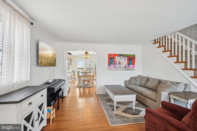 living room with stairs, ceiling fan, light wood-style flooring, and crown molding