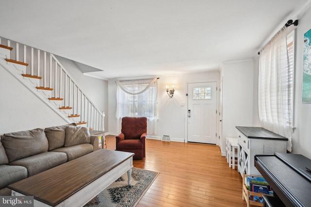 living area featuring light wood-style floors, visible vents, baseboards, and stairs