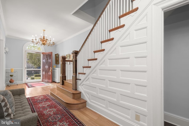 stairway featuring a notable chandelier, wood finished floors, and ornamental molding