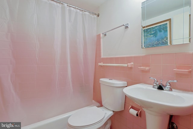 bathroom with a wainscoted wall, tile walls, shower / bath combination with curtain, toilet, and a sink