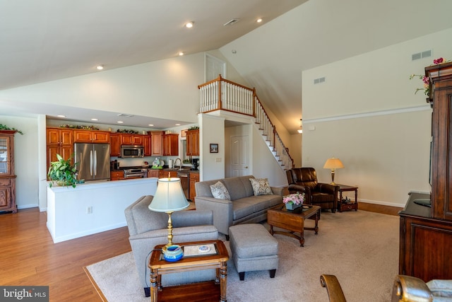 living area with high vaulted ceiling, visible vents, baseboards, stairway, and light wood-type flooring