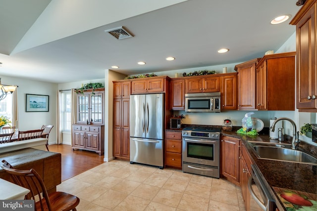 kitchen with brown cabinets, stainless steel appliances, dark countertops, recessed lighting, and a sink