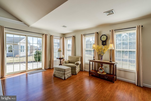 living area with vaulted ceiling, wood finished floors, visible vents, and baseboards