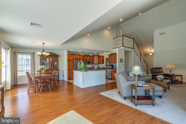 living room featuring high vaulted ceiling, light wood finished floors, visible vents, a chandelier, and baseboards