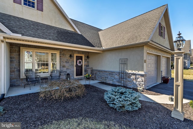 view of front facade featuring a porch, a shingled roof, stone siding, driveway, and stucco siding