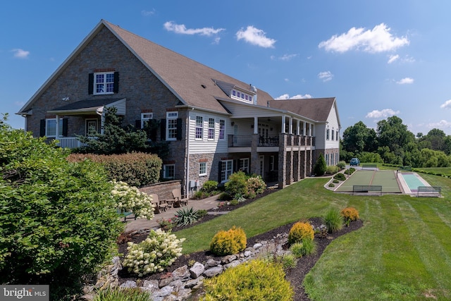 rear view of property featuring stone siding, a patio area, a ceiling fan, and a yard