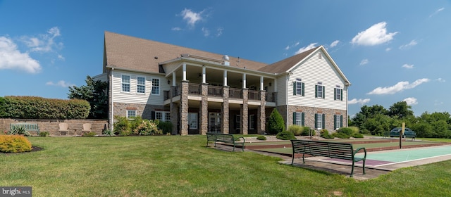 back of property with a balcony, stone siding, and a lawn