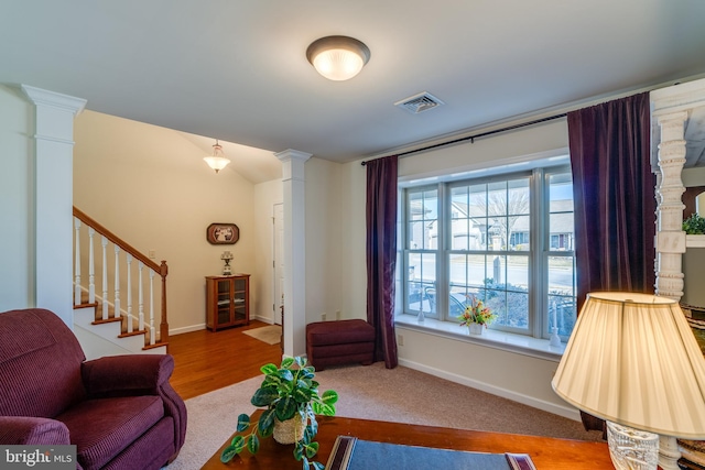 carpeted living area with stairway, decorative columns, visible vents, and baseboards