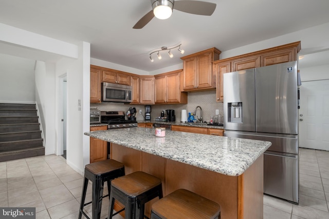 kitchen with light stone counters, light tile patterned floors, decorative backsplash, appliances with stainless steel finishes, and a center island