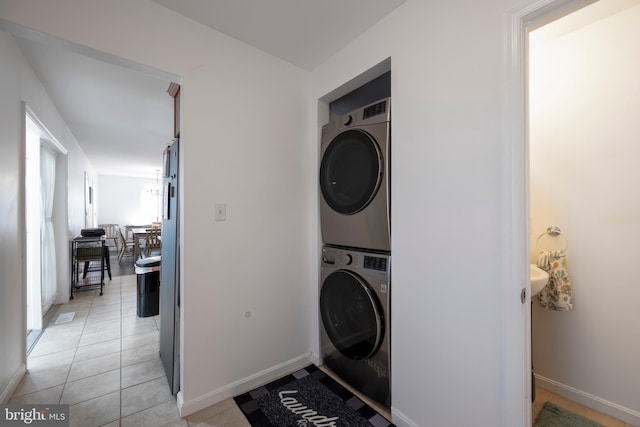 clothes washing area with laundry area, stacked washer / dryer, light tile patterned flooring, and baseboards