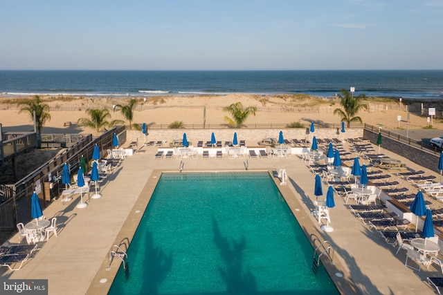 view of swimming pool with a patio area, a water view, a view of the beach, and fence