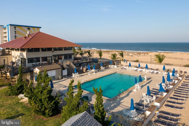 pool featuring a beach view, a water view, a patio area, and fence