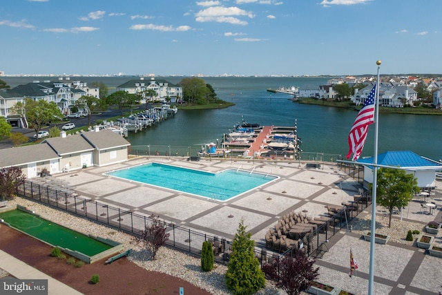 community pool with a patio area, a water view, and fence