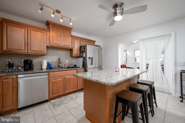 kitchen featuring a center island, a kitchen breakfast bar, light tile patterned flooring, stainless steel appliances, and a sink