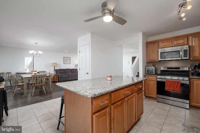 kitchen with light tile patterned floors, light stone countertops, decorative backsplash, appliances with stainless steel finishes, and a center island