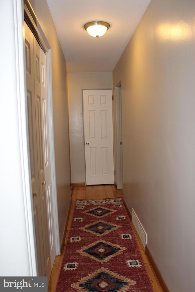 hall featuring baseboards, visible vents, and light wood finished floors