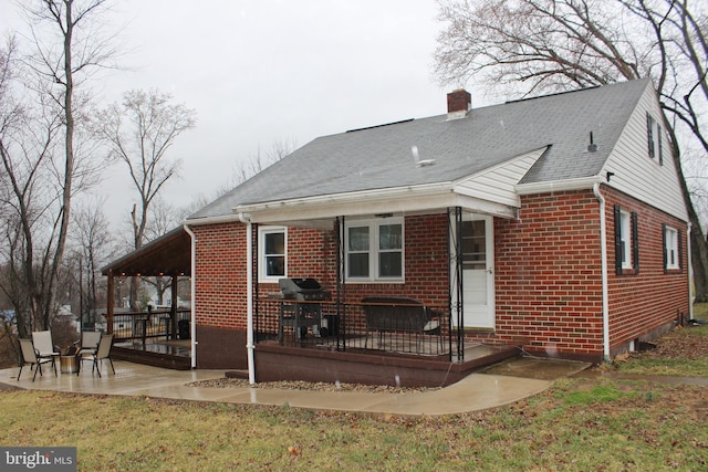 rear view of house featuring brick siding, a lawn, a chimney, and a patio