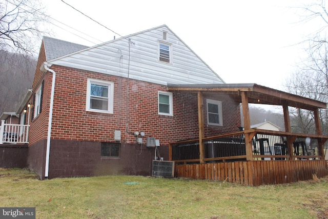 back of property featuring brick siding, a lawn, cooling unit, and roof with shingles