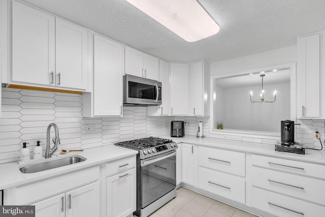 kitchen with decorative backsplash, appliances with stainless steel finishes, white cabinets, a sink, and a textured ceiling