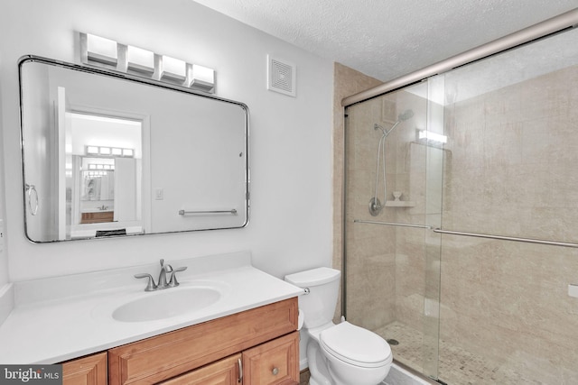 bathroom featuring a textured ceiling, toilet, vanity, visible vents, and a stall shower