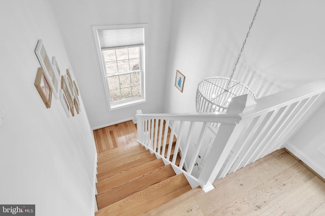 staircase with baseboards, wood finished floors, and an inviting chandelier