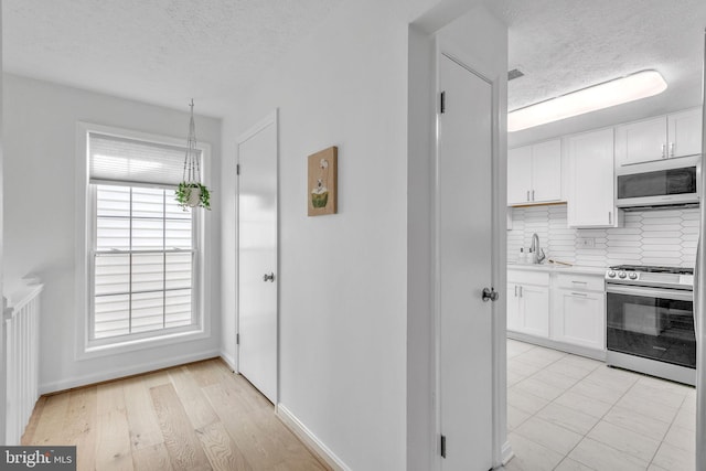 kitchen featuring tasteful backsplash, white microwave, stainless steel gas range, and white cabinets