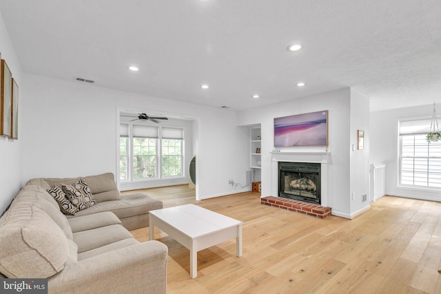 living room featuring light wood-type flooring, a brick fireplace, visible vents, and recessed lighting