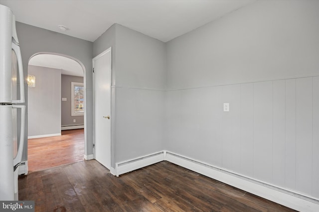 spare room featuring arched walkways, baseboard heating, a baseboard radiator, and wood finished floors