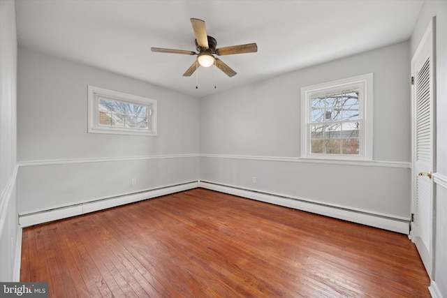 unfurnished bedroom featuring multiple windows, a baseboard heating unit, and hardwood / wood-style floors