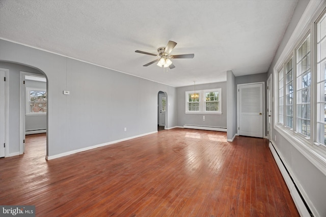 unfurnished room featuring arched walkways, hardwood / wood-style floors, baseboard heating, and a ceiling fan