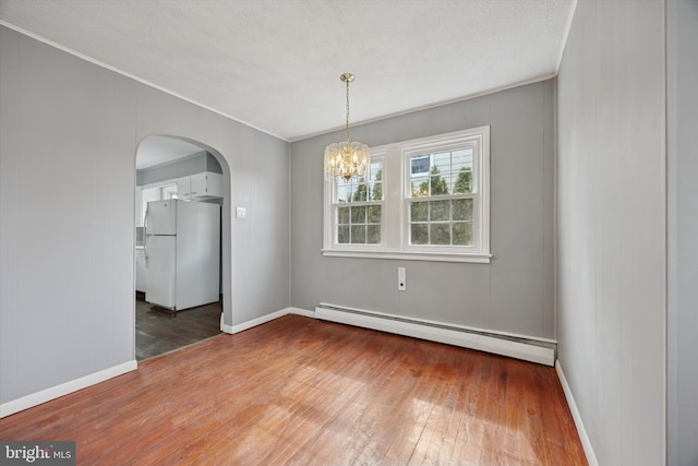 unfurnished dining area with arched walkways, wood-type flooring, an inviting chandelier, a baseboard heating unit, and baseboards