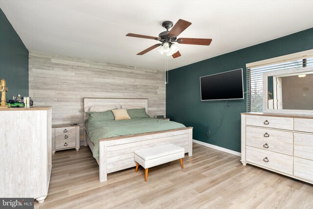 bedroom featuring ceiling fan, baseboards, light wood-style flooring, and an accent wall