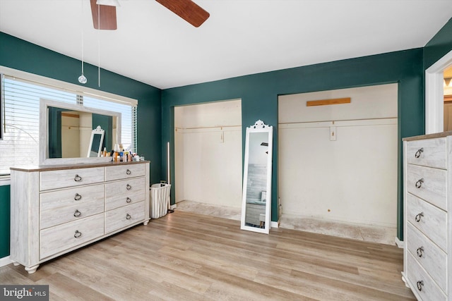 bedroom featuring light wood finished floors, a ceiling fan, and multiple closets