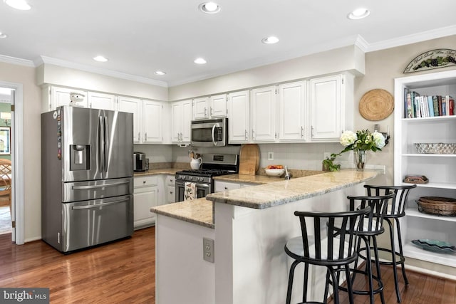 kitchen featuring light stone counters, dark wood-style flooring, a peninsula, stainless steel appliances, and white cabinetry