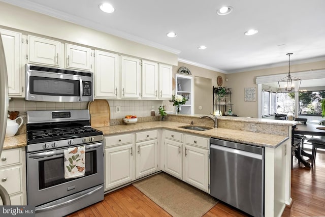 kitchen featuring appliances with stainless steel finishes, light wood-style floors, ornamental molding, a sink, and a peninsula