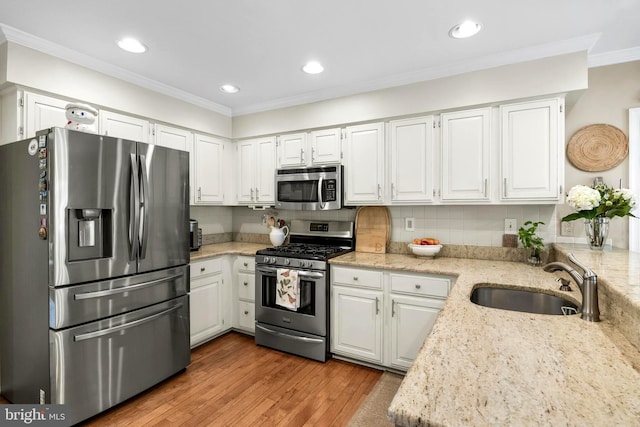 kitchen featuring stainless steel appliances, light wood-style flooring, ornamental molding, white cabinets, and a sink