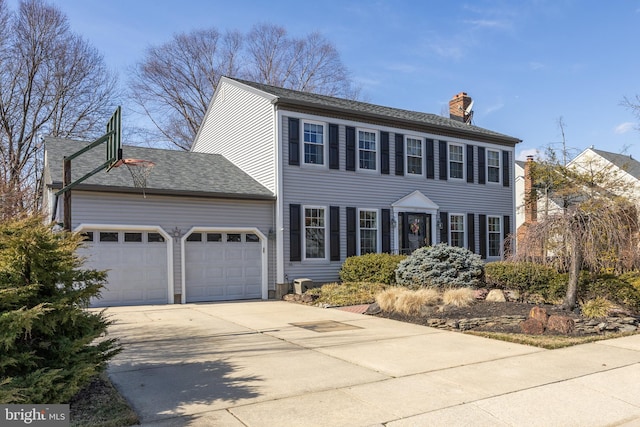 colonial-style house featuring a garage, driveway, and a chimney