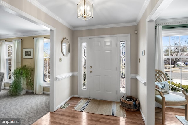 entryway with a notable chandelier, visible vents, baseboards, hardwood / wood-style floors, and crown molding